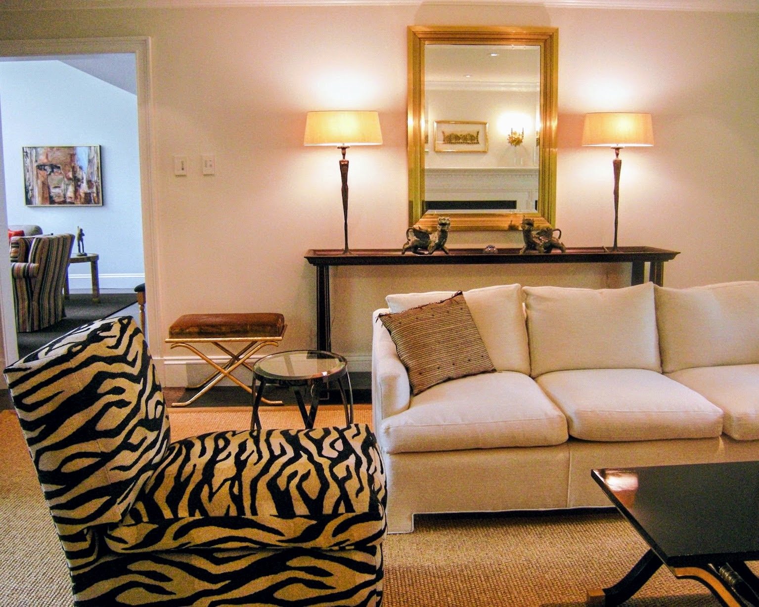 Living room with a white sofa, a zebra-print slipper chair, a gilt mirror, and a pair of sculptural table lamps