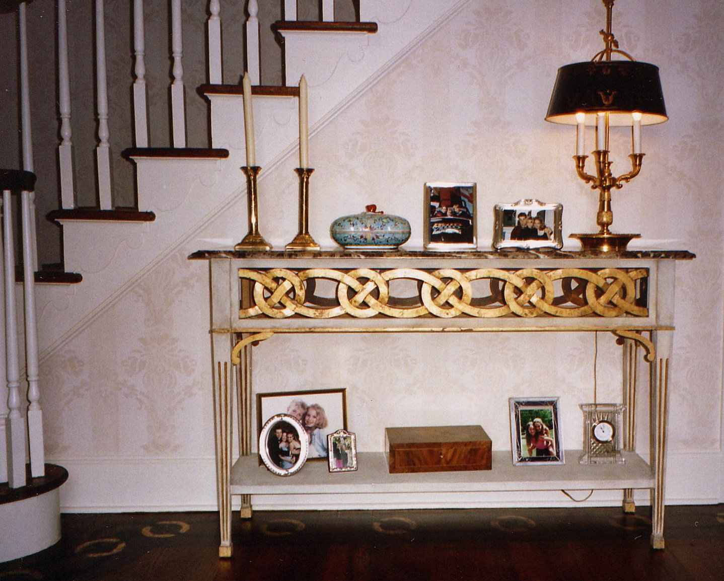 Entry vignette with a gilded fretwork console, a tole bouillotte lamp, and framed photographs