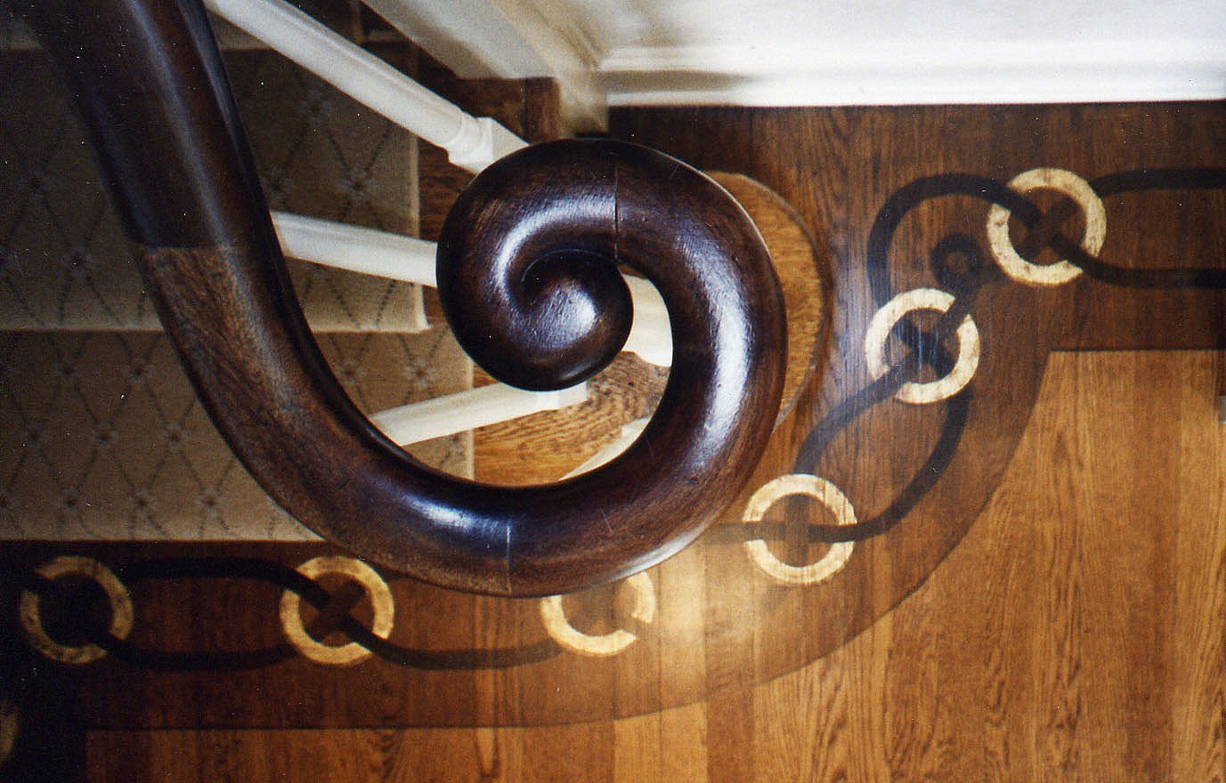 Hand-carved stair volute above a custom chain-motif hardwood floor inlay