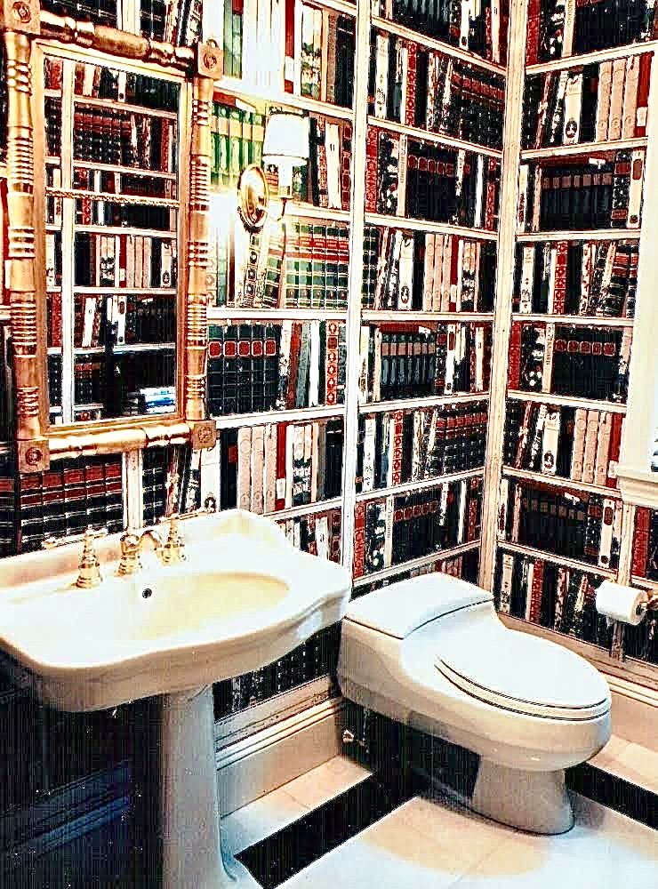 Powder room wrapped in library-spine wallpaper with a bamboo mirror and a pedestal sink