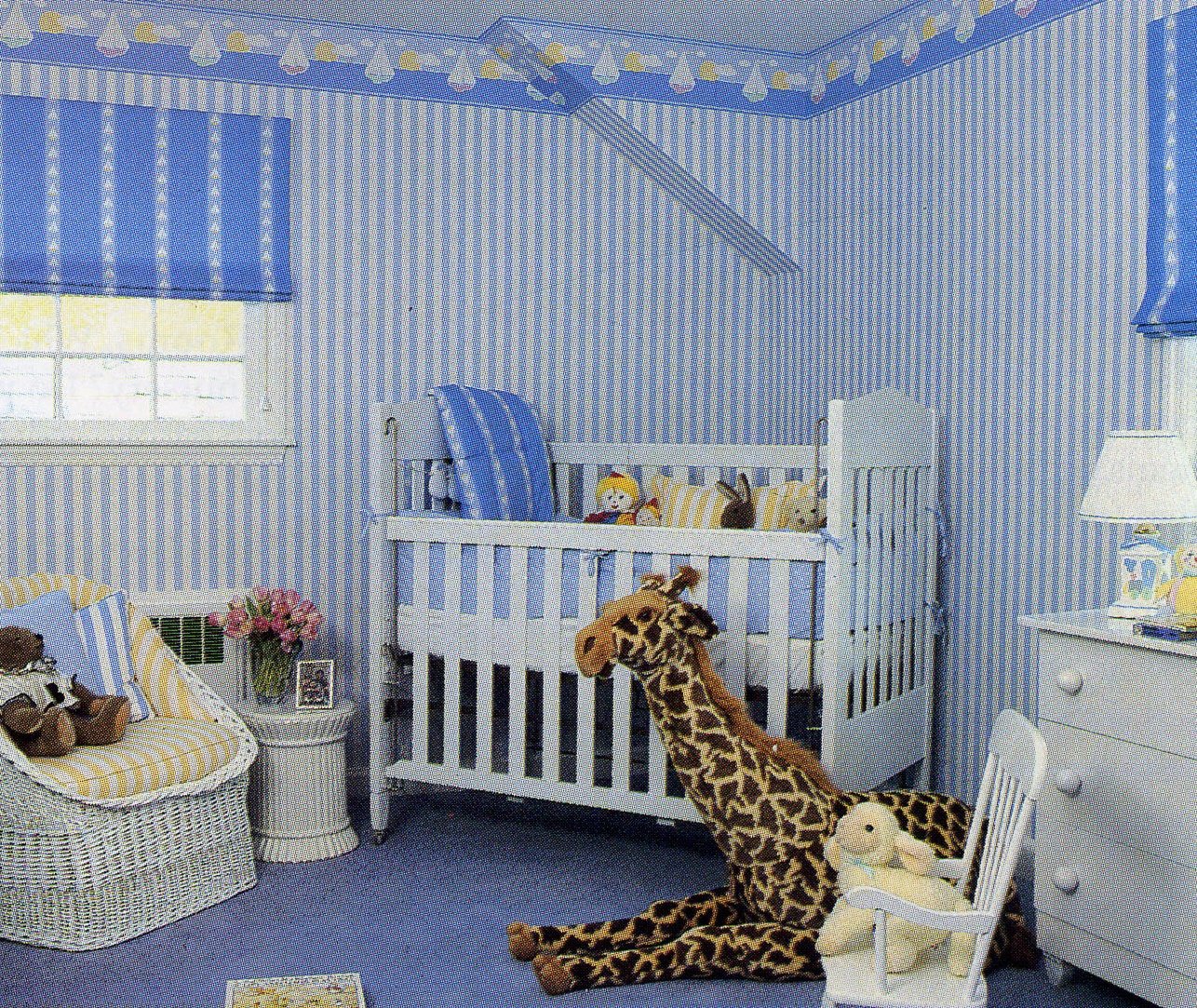 Blue-striped nursery with a white crib, a sailboat wallpaper border, and a plush giraffe
