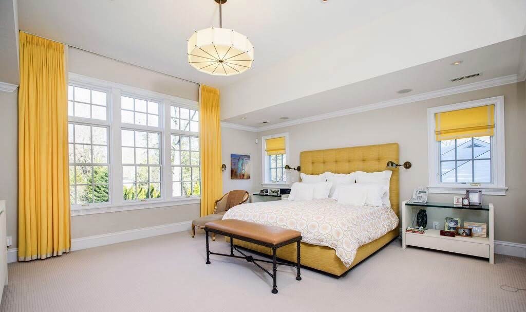 Serene primary bedroom with a saffron upholstered bed, silk drapery, and a drum pendant