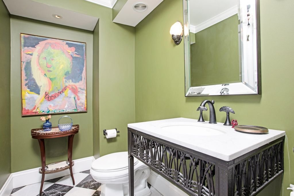 Green powder room with an abstract portrait, an iron vanity, and a checkerboard marble floor