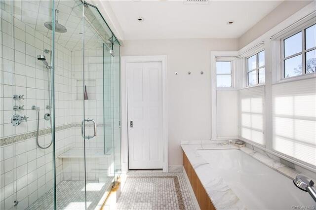 Marble primary bath with a frameless glass shower and a soaking tub beneath the window
