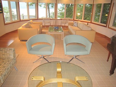 Lakeside sunroom with pale sofas, swivel chairs, and walls of windows