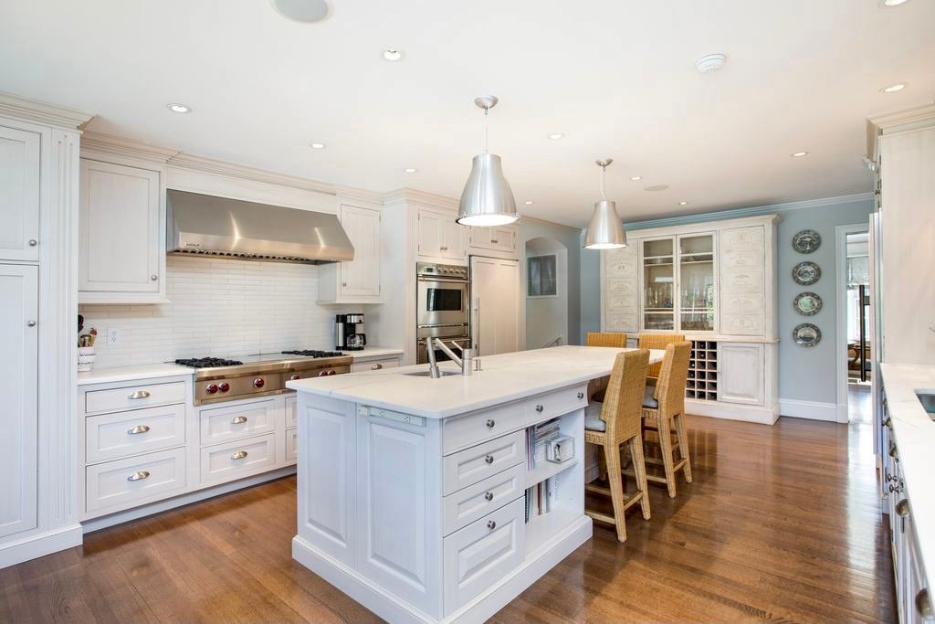 White kitchen with pewter pendants, glass-front cabinetry, and a marble-topped island