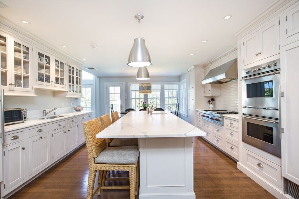 Bright white kitchen with a marble island, professional range, and polished nickel pendants