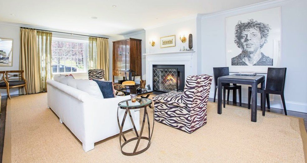 Bright living room with a white sofa and zebra-print chairs arranged around a fireplace beneath a charcoal portrait
