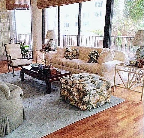 Coastal condominium living room with a floral ottoman and a shaded terrace beyond
