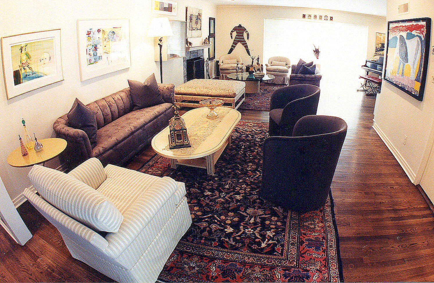 Art-filled living room with a tufted sofa, swivel barrel chairs, and a hand-knotted oriental rug